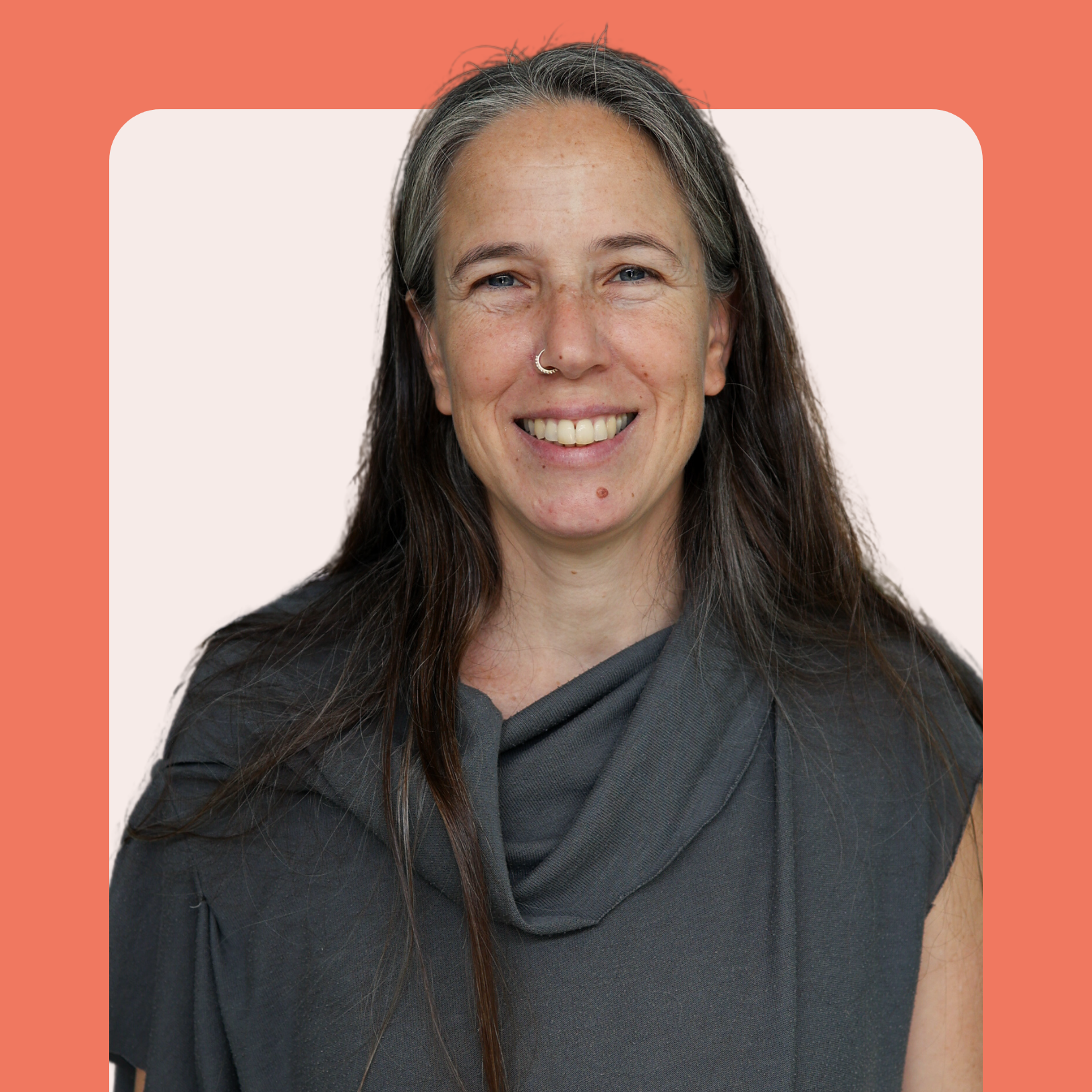 A smiling woman with long brown hair and a nose ring wears a gray top. She stands in front of a pale background framed by a coral border with rounded corners.