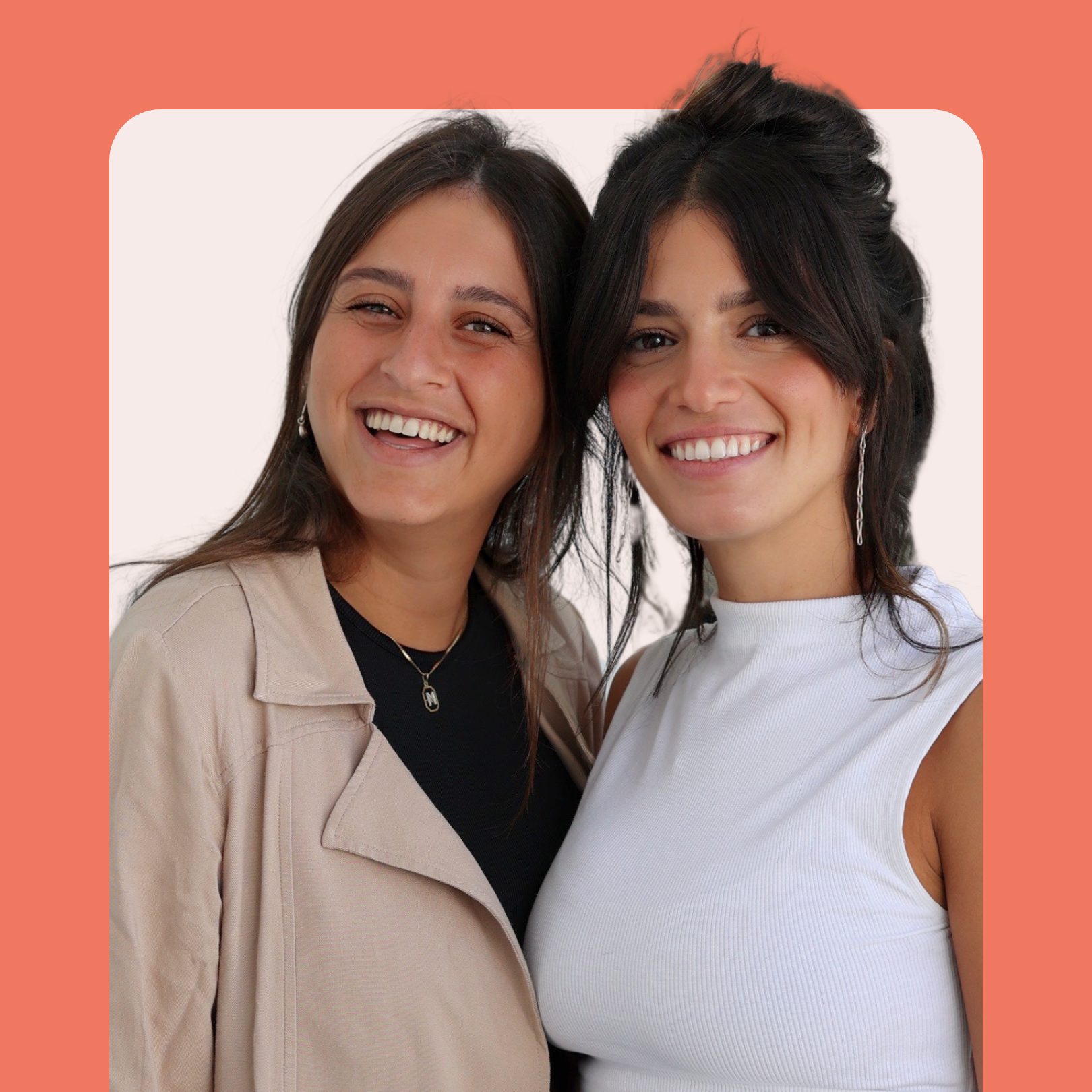 Two women smiling and standing close together in front of a peach-colored background with rounded corners, one wearing a beige jacket and the other in a sleeveless white top.