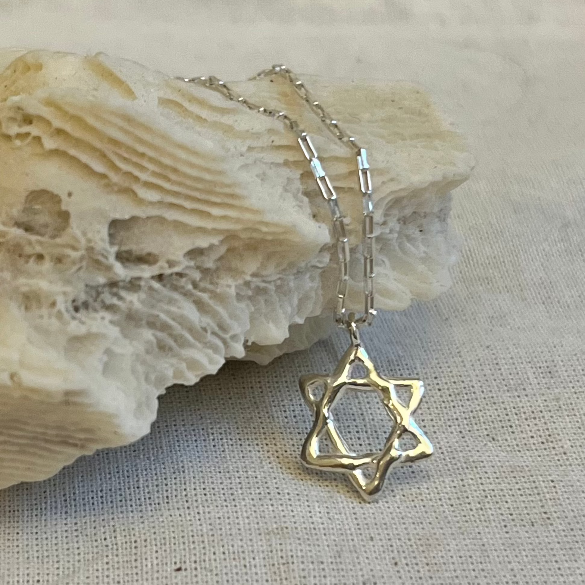 Sterling silver Star of David necklace with organic textured design on chain displayed on natural stone background