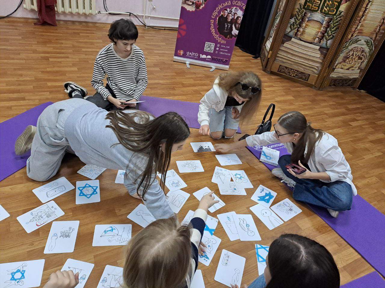 Participants engaging with David Cards Israel Education Card Set, featuring various illustrated cards spread on a wooden floor.