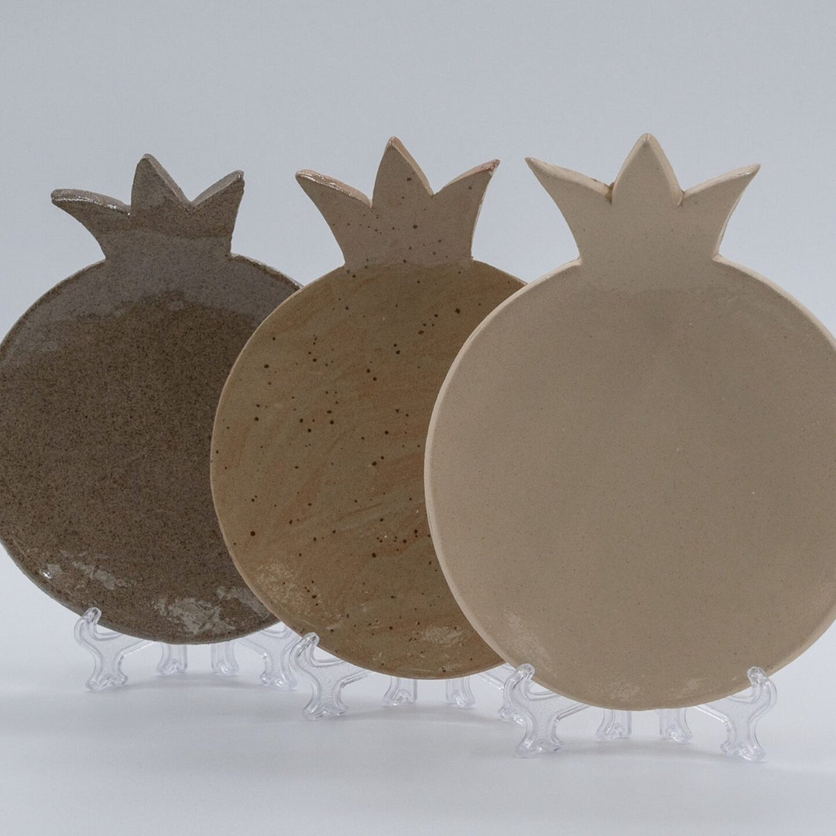 ADI Pomegranate Plates, three ceramic pomegranate-shaped plates in dark brown, speckled tan, and cream finishes.