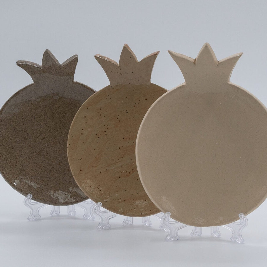 ADI Pomegranate Plates, three ceramic pomegranate-shaped plates in dark brown, speckled tan, and cream finishes.