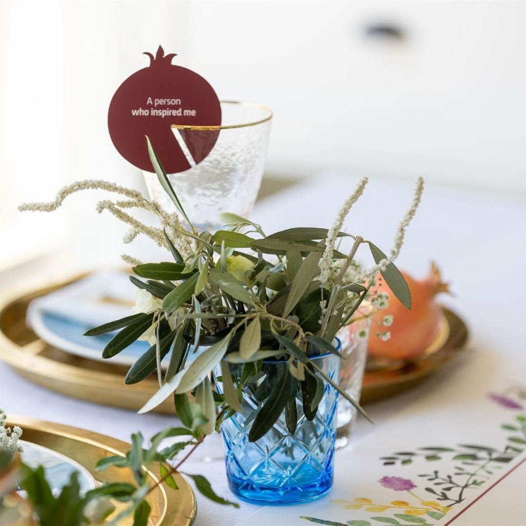 Pomegranate-shaped Family Game conversation starter card on glass with decorative greenery on festive table setting