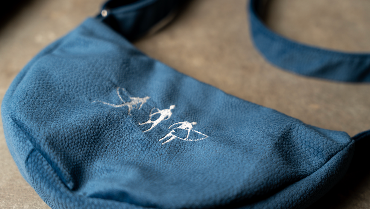 Blue hand sewn suede shoulder bag with white embroidered surfers design and adjustable strap