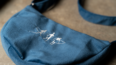 Handmade Embroidered Shoulder Bag in textured blue fabric, with delicate white figures and surfboards stitched on the front.