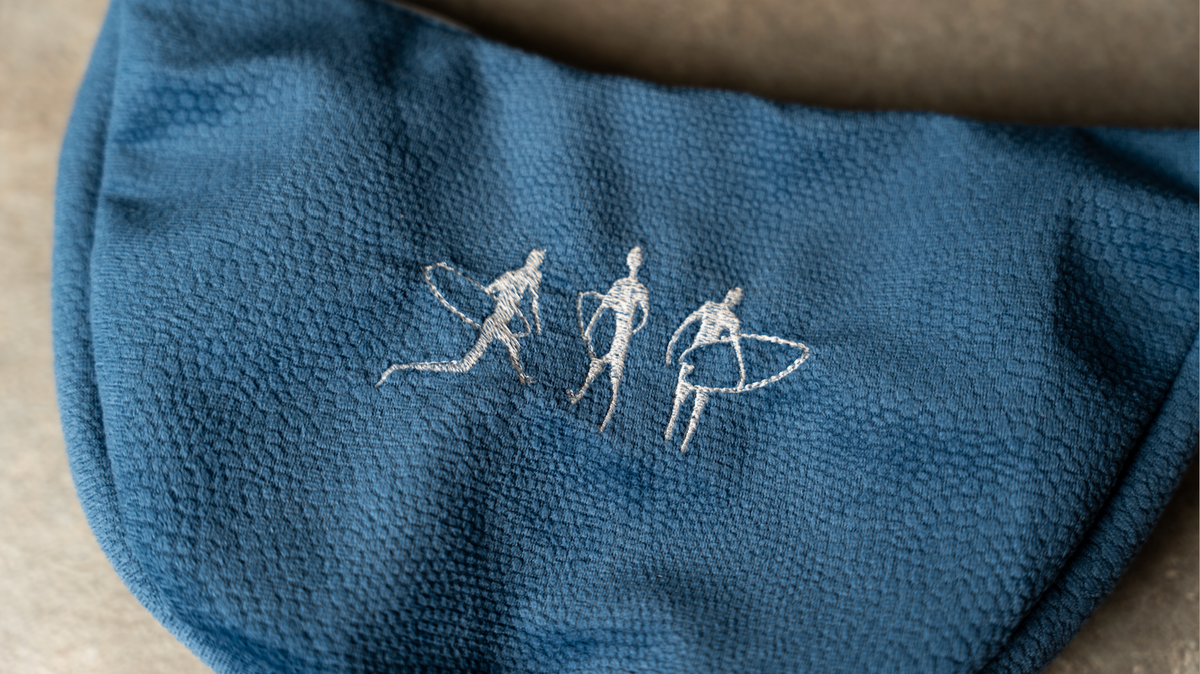Handmade Embroidered Shoulder Bag in textured blue fabric, featuring white stitched figures with surfboards.