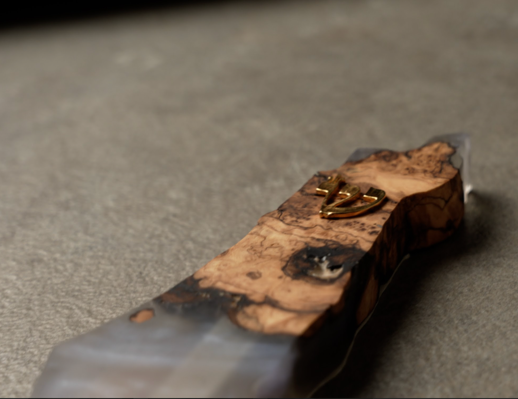 Handmade epoxy and olivewood mezuzah with natural wood grain and gold Hebrew letter on textured surface