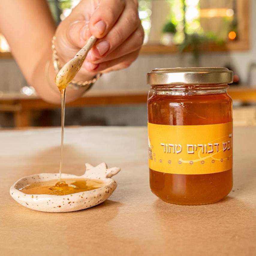 Handcrafted ceramic pomegranate-shaped honey dish with glossy glaze and speckled stoneware, shown with honey jar and honey dipper dripping honey.
