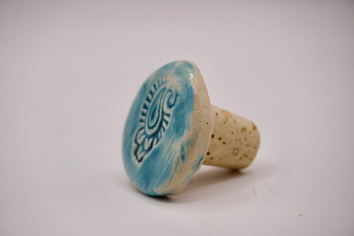 Bottle stopper with an ADI Hand-Painted Ceramic turquoise top, dark swirling motif, and natural cork base dotted with speckles.