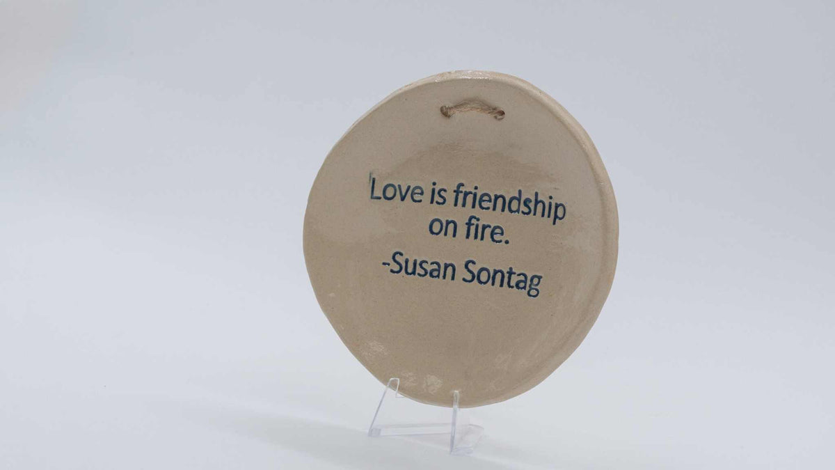 ADI Inspirational Quote Hanging Plate, round beige ceramic plaque with blue Susan Sontag quote and hanging slot