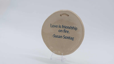 ADI Inspirational Quote Hanging Plate, round beige ceramic plaque with blue Susan Sontag quote and hanging slot