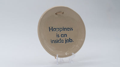 ADI Inspirational Quote Hanging Plate, round beige ceramic plaque with blue “Happiness is an inside job” lettering and hanging loop