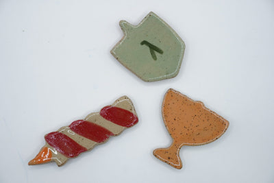 ADI Chanukah Magnet Set featuring three speckled ceramic magnets: a green dreidel, red-and-white candle, and orange oil jug.