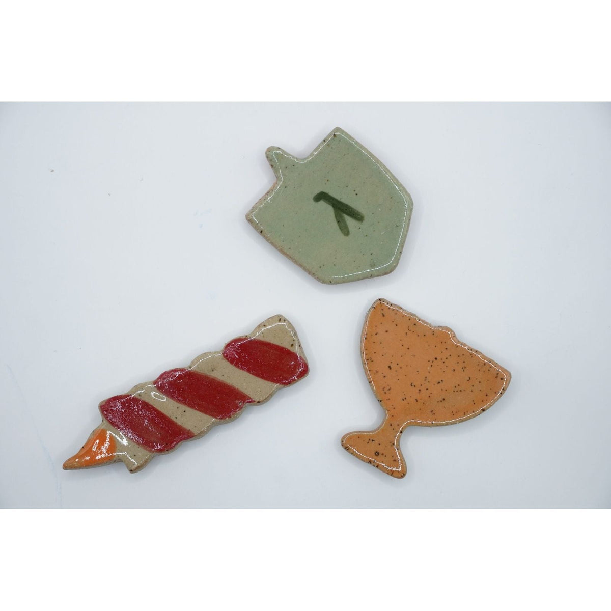ADI Chanukah Magnet Set features three speckled ceramic magnets: a green dreidel, red-and-cream candle, and orange oil jug.