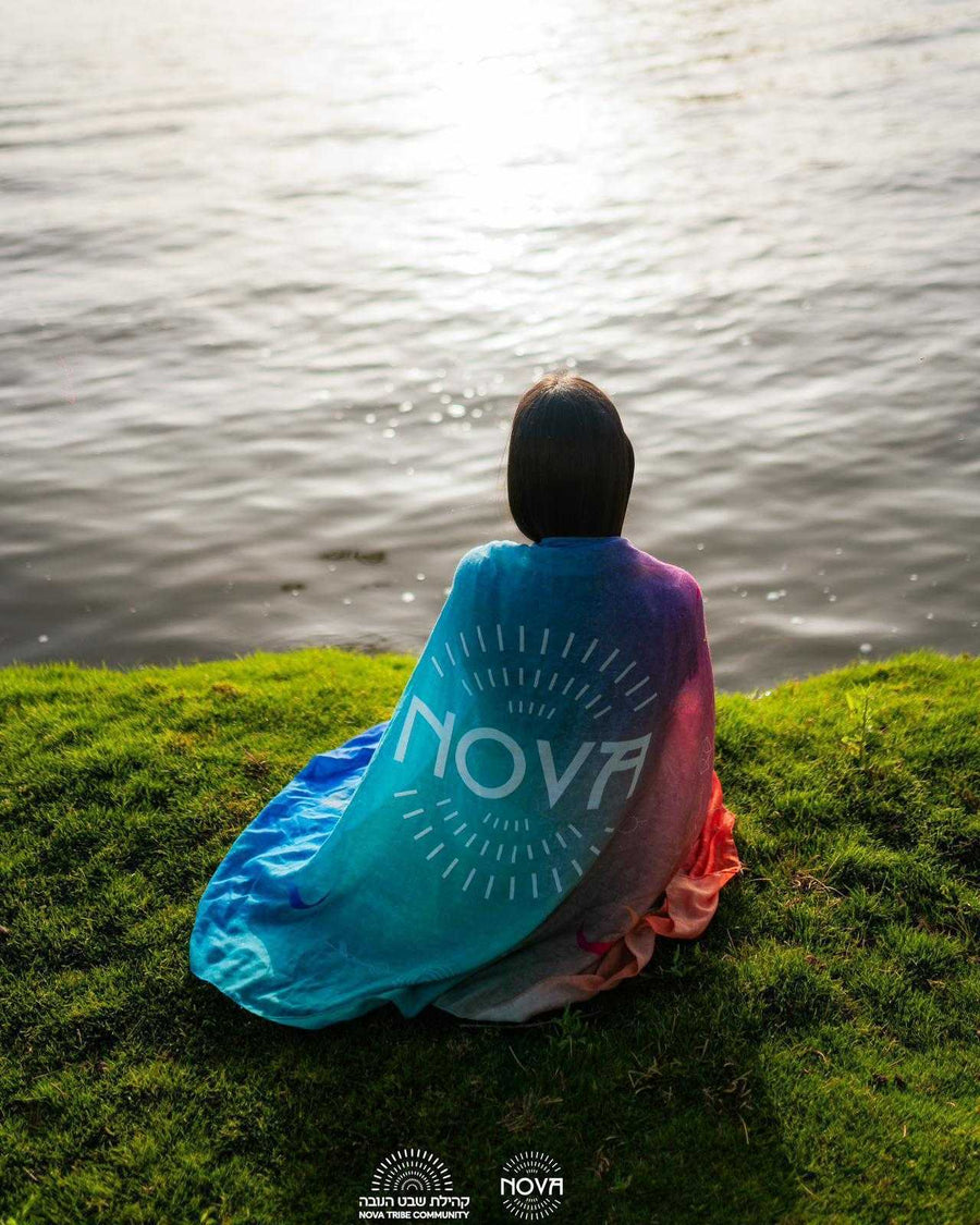 Nova Shawl in multicolor cotton, draped over the shoulders with a large Nova logo and radiating line pattern.
